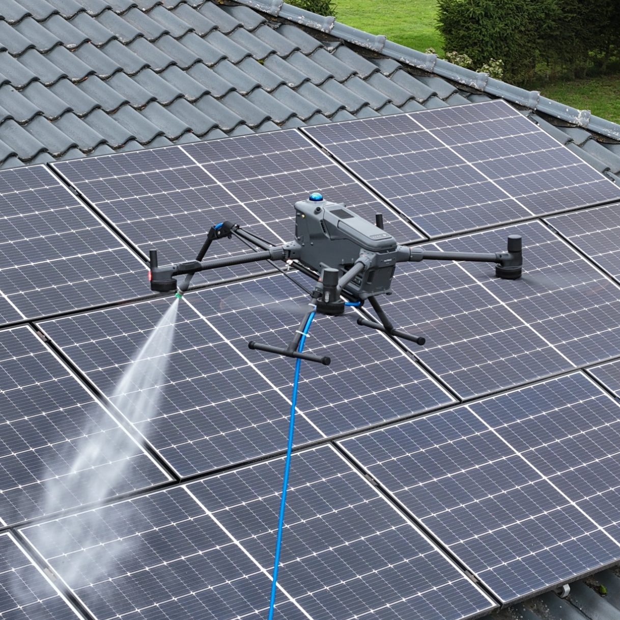 Drohne Reinigung Ein Drohne sprüht Wasser über Solarpanels auf einem Dach.